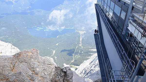 Absturzhöhe veranschaulicht durch einen Mann, der auf einem Gebäude in den Bergen steht.