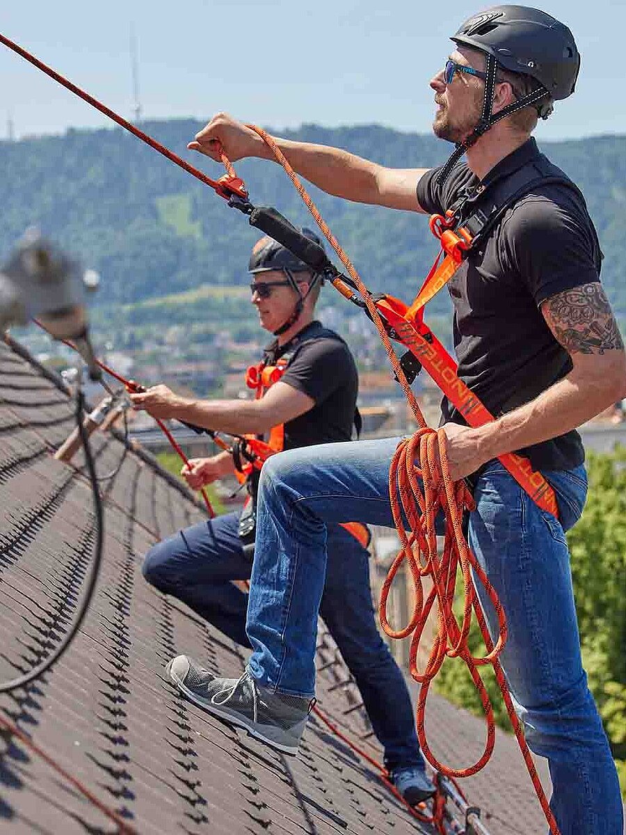 Twee geschoolde arbeiders op een hellend dak met een INNOTECH beveiligings- en valbeveiligingssysteem